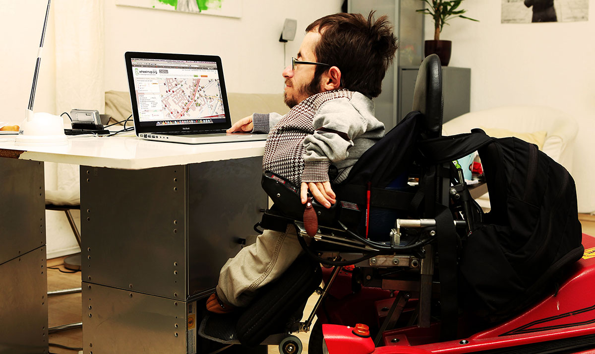Acessibilidade: usuário com deficiências físicas sentado em uma cadeira de rodas, utilizando um notebook conectado à internet.