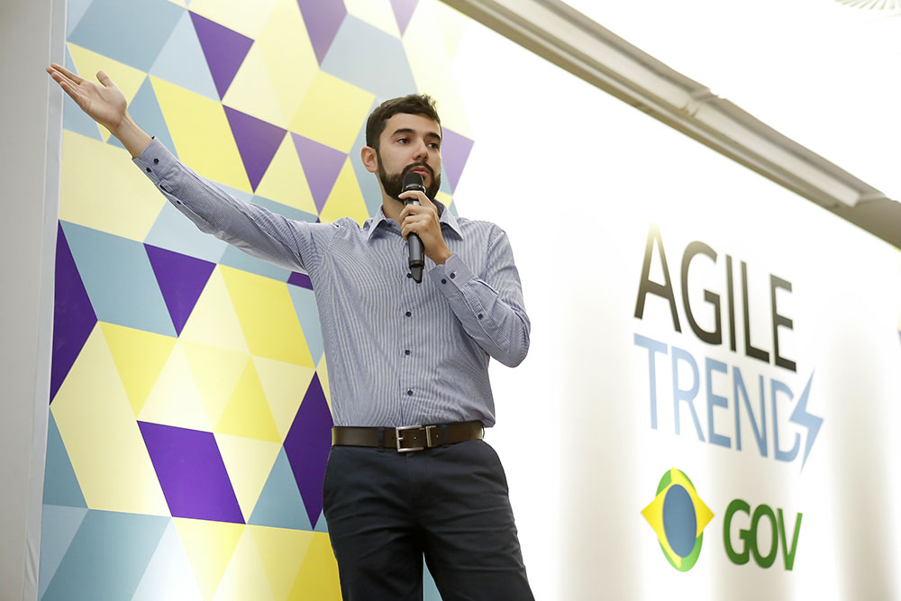 Thiago Nascimento segurando o microfone, com as mãos erguidas, palestrando no Agile Trends Gov 2018