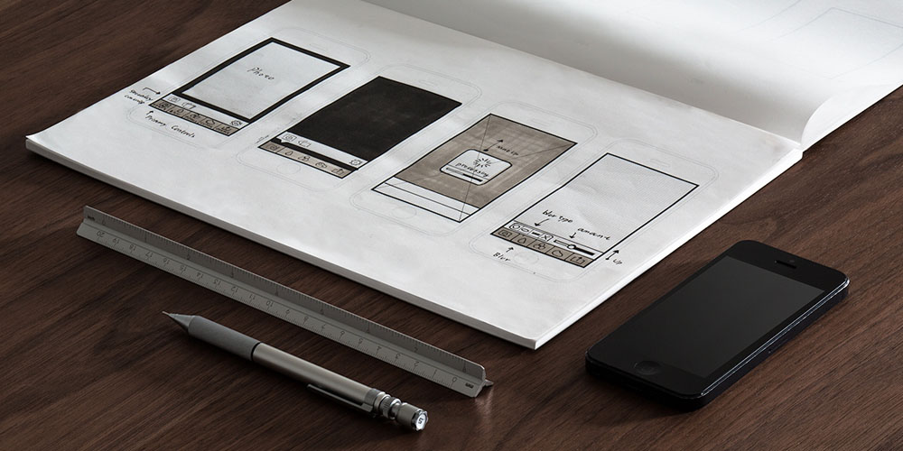 Protótipos bem desenhados em um caderno e ao lado, caneta, régua e celular.