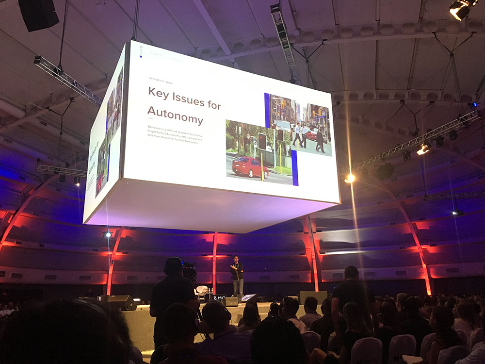 Steven Choi no centro do palco apresentando slide sobre os carros autônomos do Uber